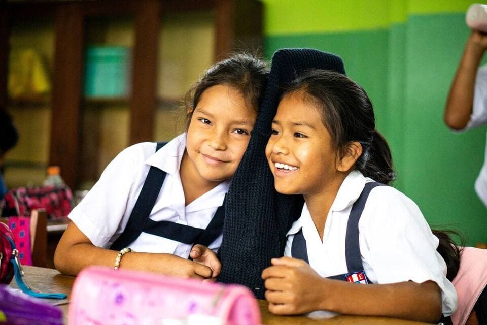 Two schoolgirls in uniform laughing together in a classroom