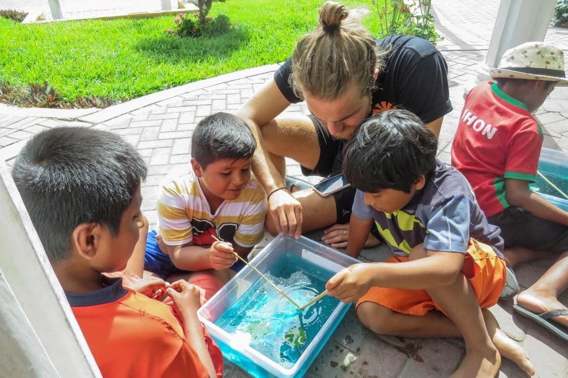 A volunteer leading an outdoor lesson with children gathered around a tray of water