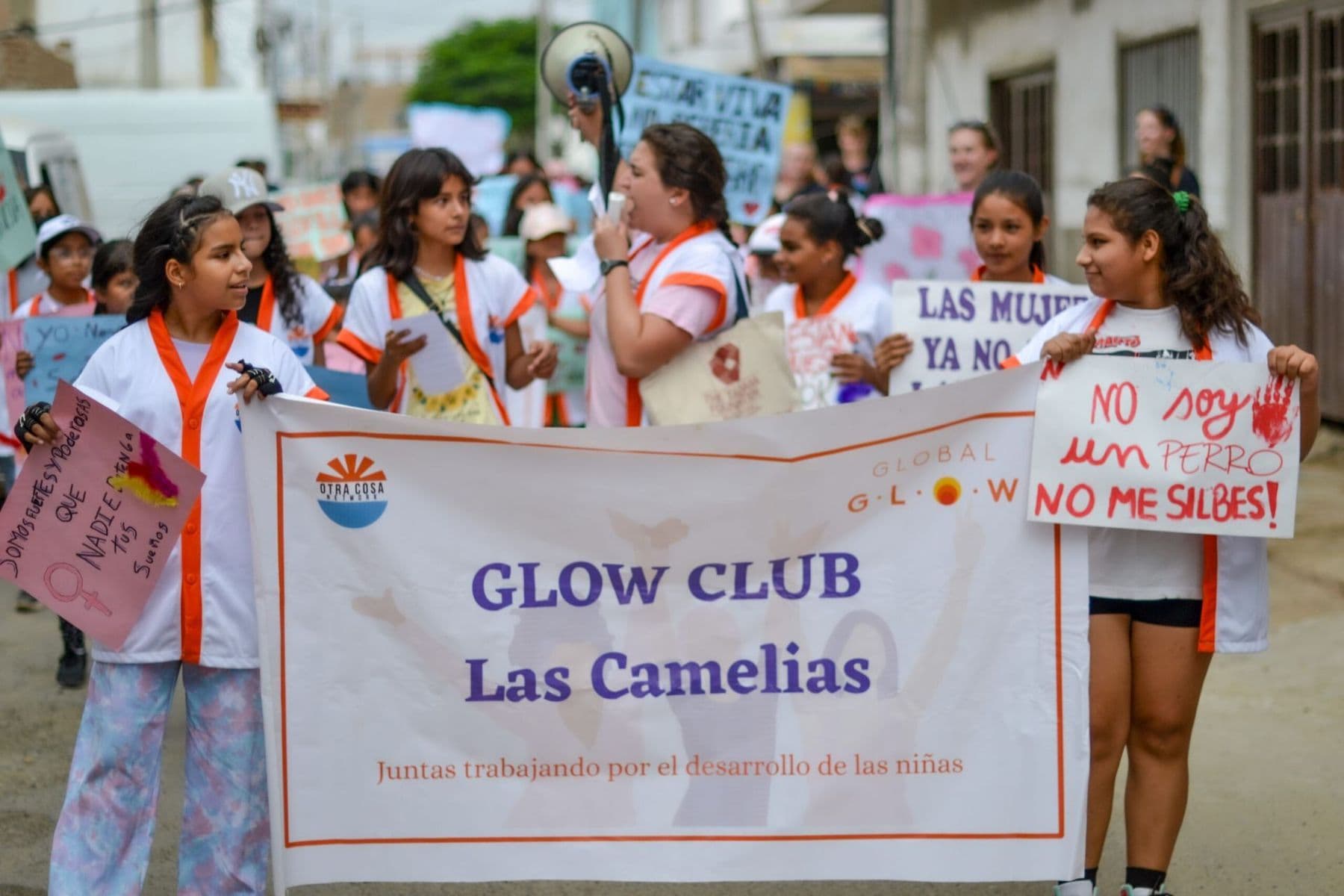 Girls holding a GLOW Club Las Camelias banner and hand-made signs