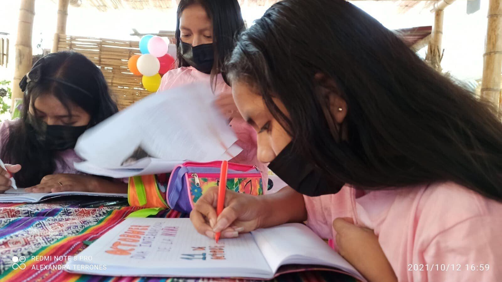 Girls writing and drawing in notebooks around a table