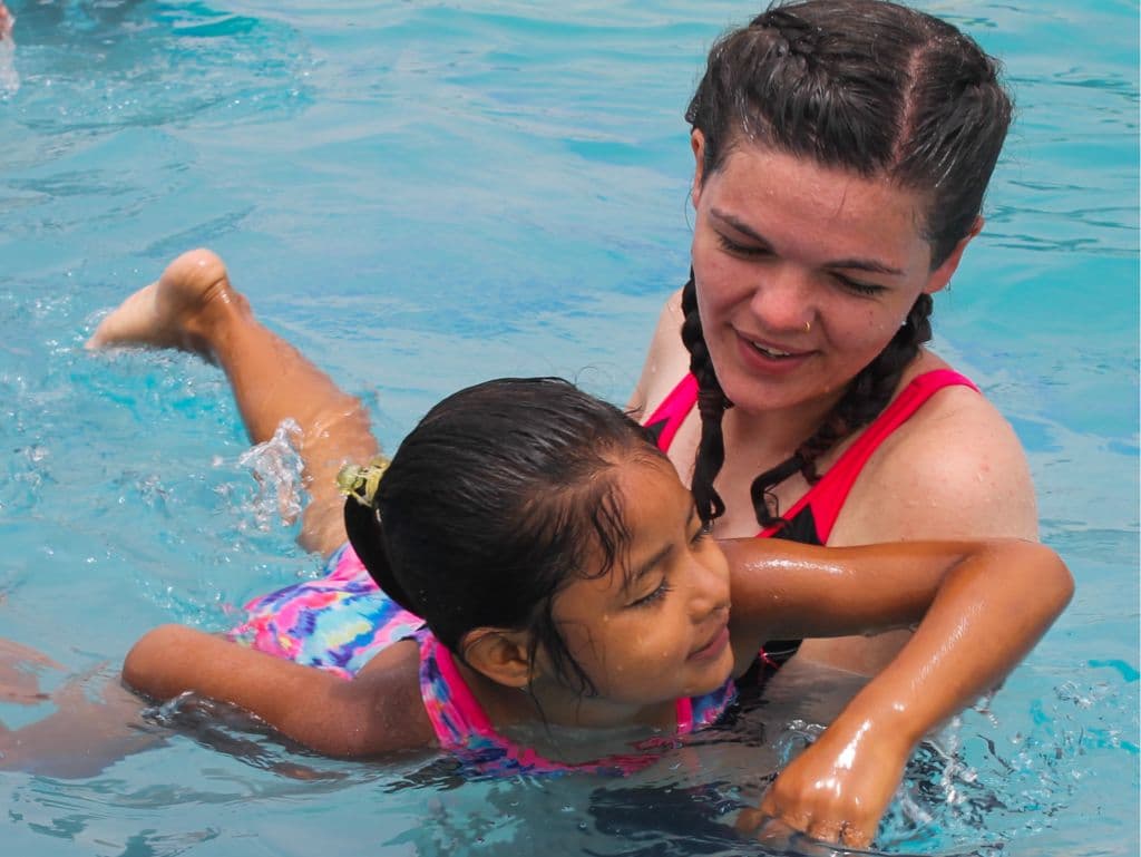 An instructor supporting a young girl as she practises floating