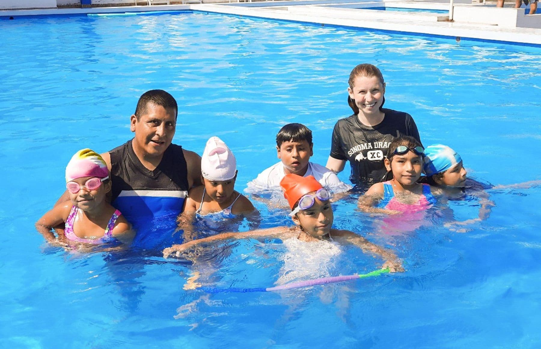 Instructors and children in swimming caps smiling together in the pool