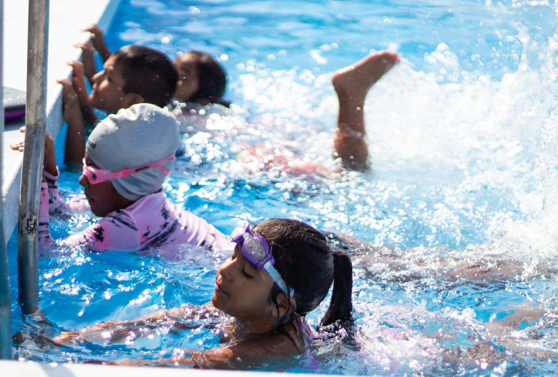Children kicking and splashing at the side of the pool