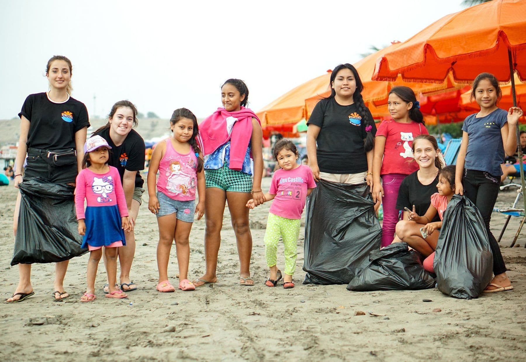 Volunteers and local children on Huanchaco beach with bags of rubbish collected during a beach clean