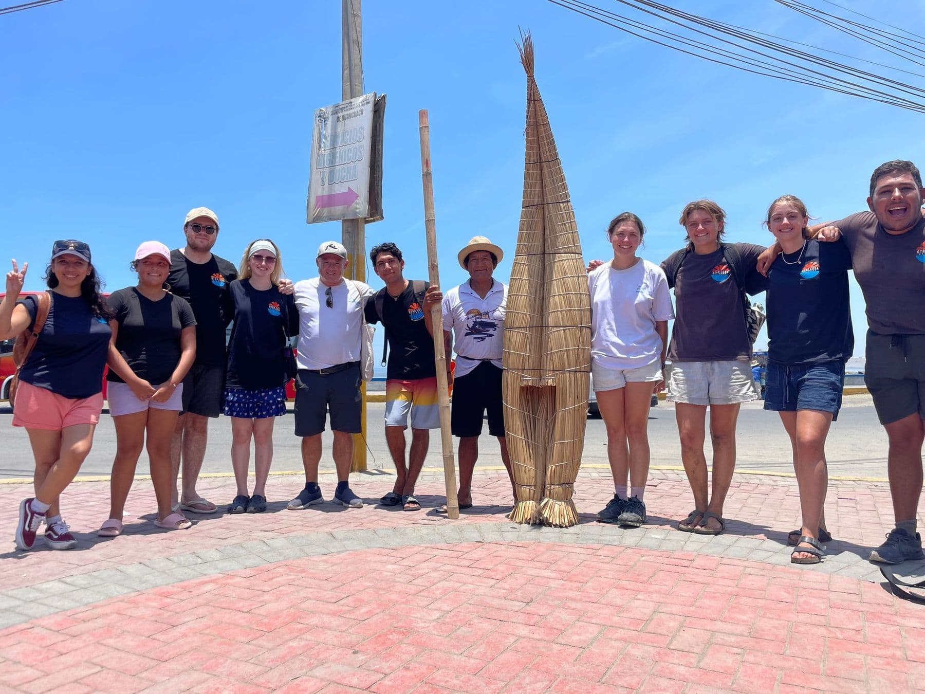 The OCN team and volunteers standing together on Huanchaco's seafront beside a traditional reed boat