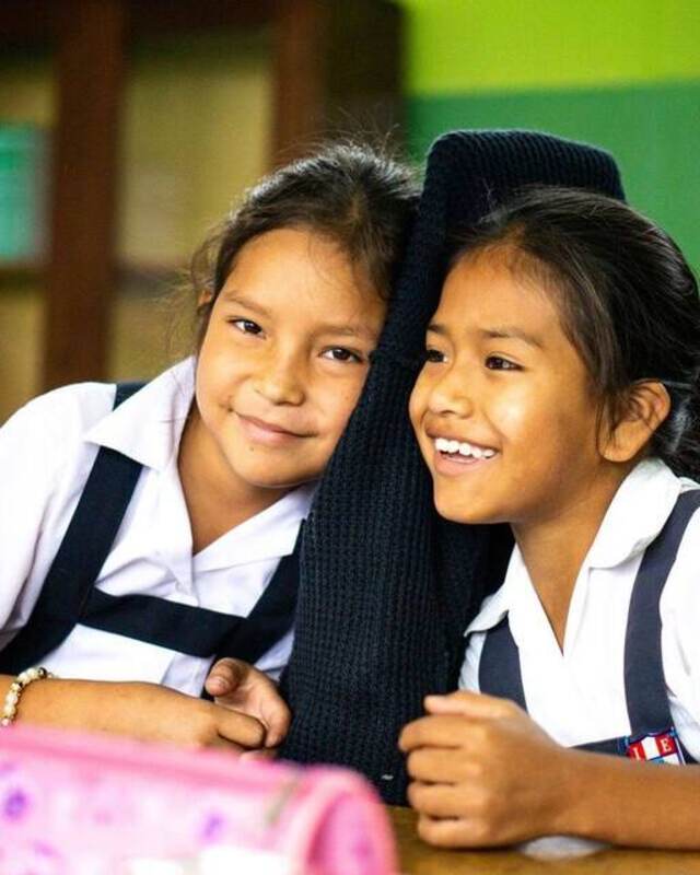 Two schoolgirls laughing together in an Otra Cosa classroom
